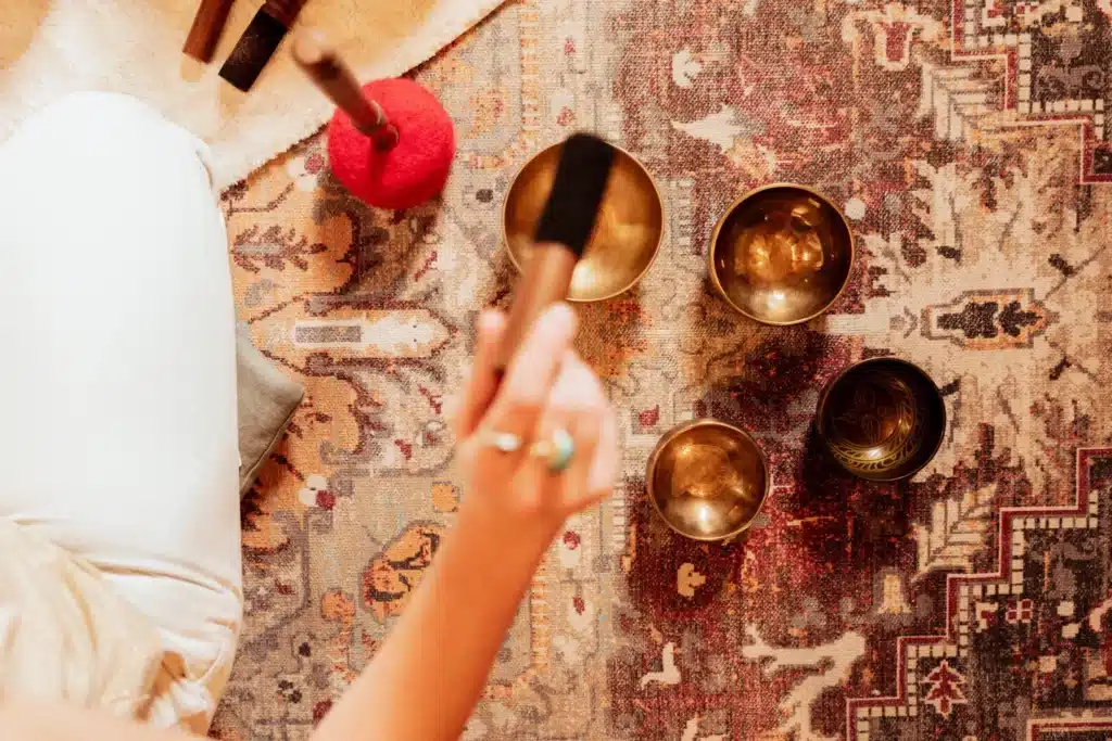 Vue de dessus de la main de Caroline s'apprêtant à faire chanter des bols tibétains disposés sur un tapis oriental.