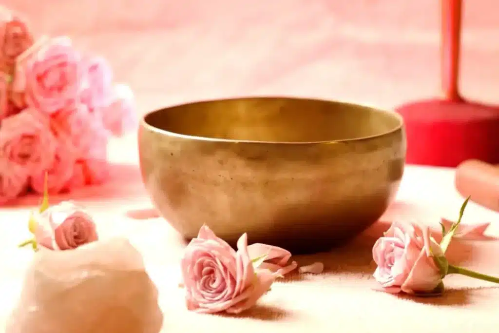 Bol chantant tibétain entouré de roses et de quartz rose, représentant la douceur et l'aspect curatif de la thérapie par le son.