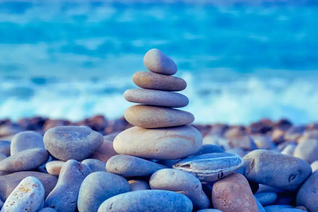 Cairn de galets gris empilés en équilibre sur une plage, avec l'océan bleu en arrière-plan, symbolisant la stabilité et la prévention du burn-out.