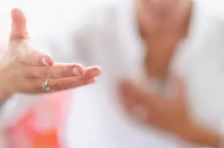 Main d'une femme tendue dans un geste d'écoute et de ressenti, avec son corps en arrière-plan flou, symbolisant la perception intuitive du taux vibratoire.