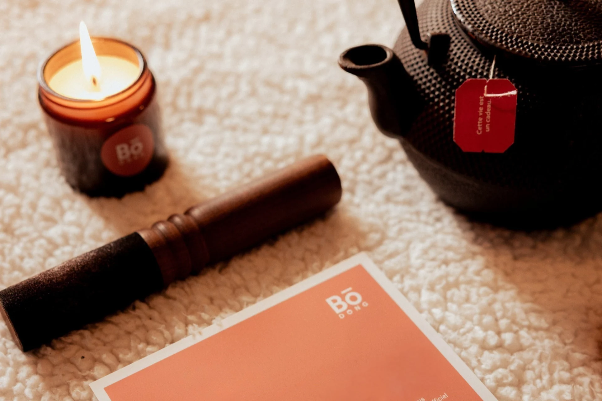 Bougie Bo-DONG allumée, théière noire et carnet sur tapis doux — rituel du matin et instant de recentrage