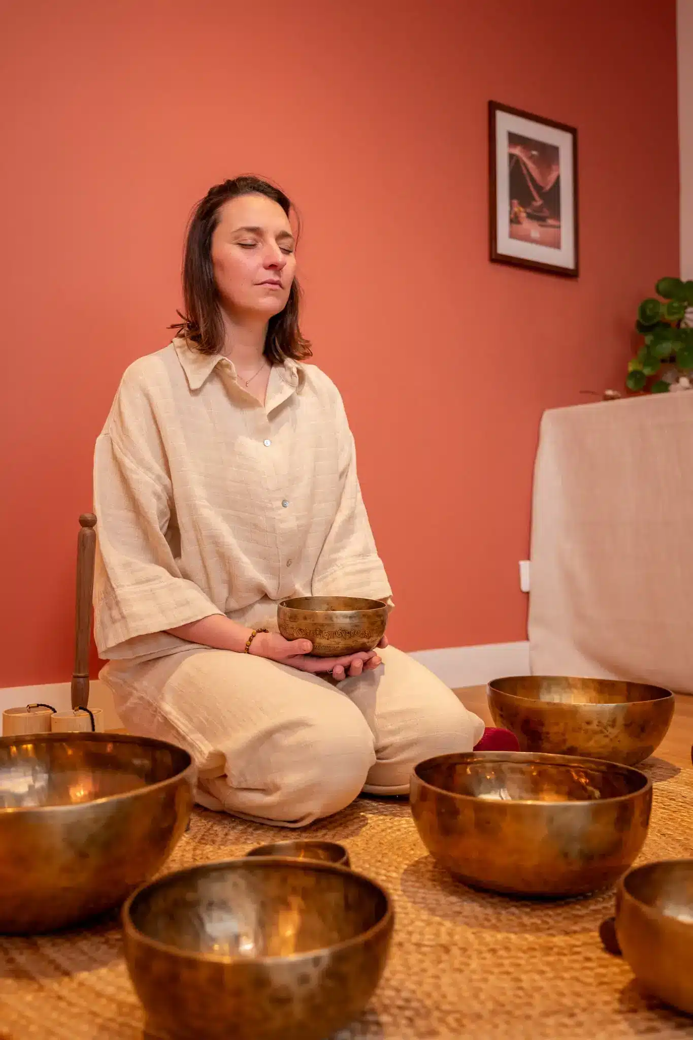 Caroline en méditation avec un bol tibétain, entourée de bols chantants dans une salle aux tons chauds